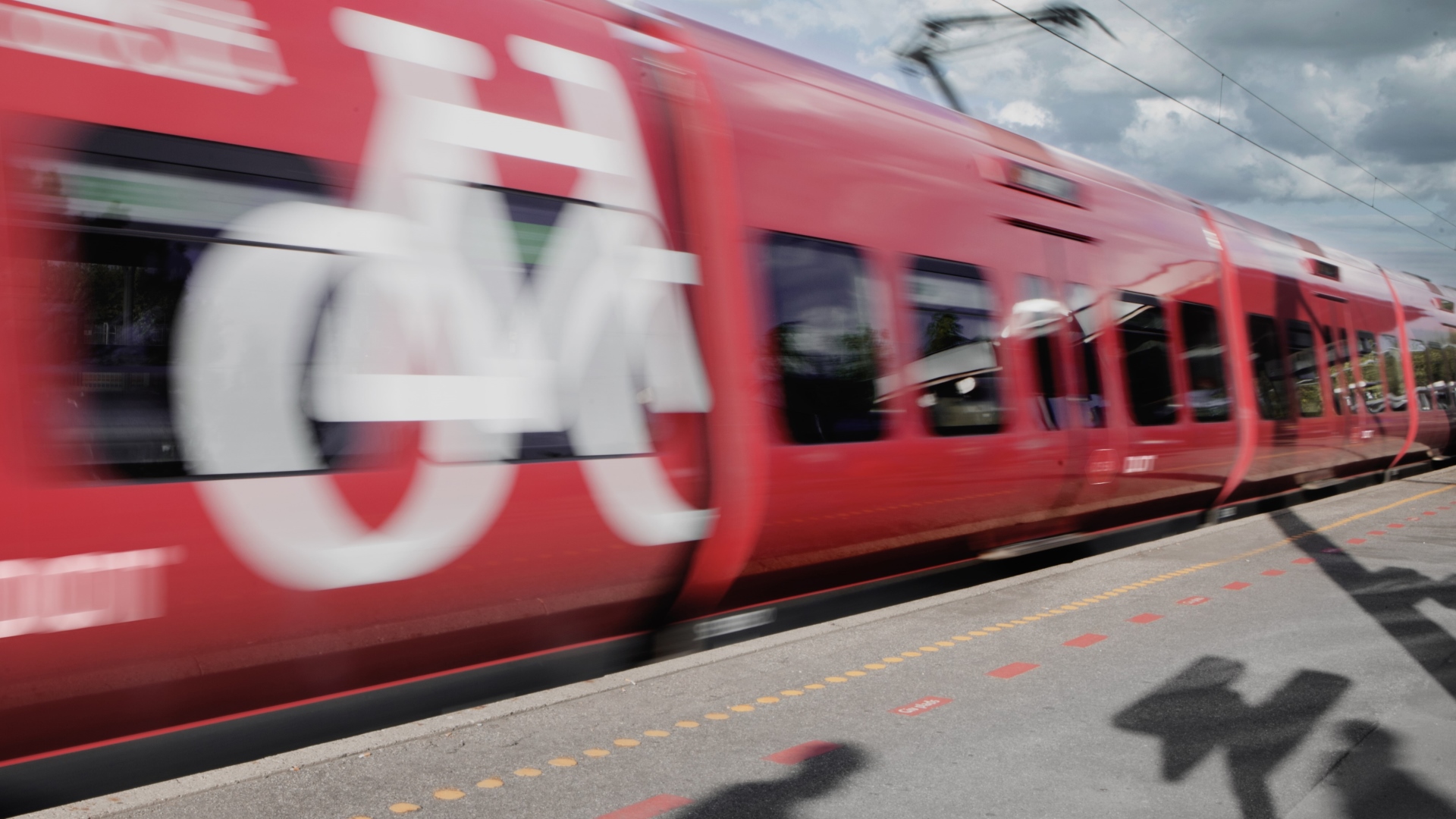 S tog kører forbi perron med skygger af passager der står og venter